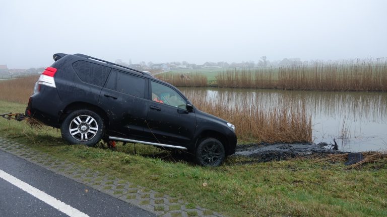 Automobilist bezig met handsfree set rijdt half te water bij Ursem