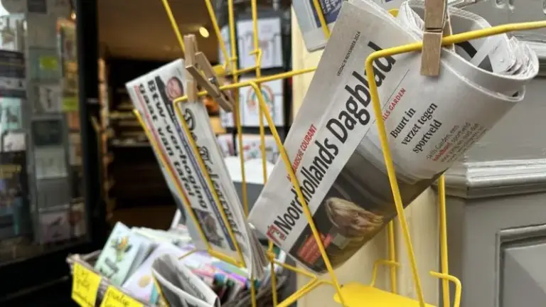 Een rek met kranten bij de ingang van een winkel, waaronder het Noordhollands Dagblad.