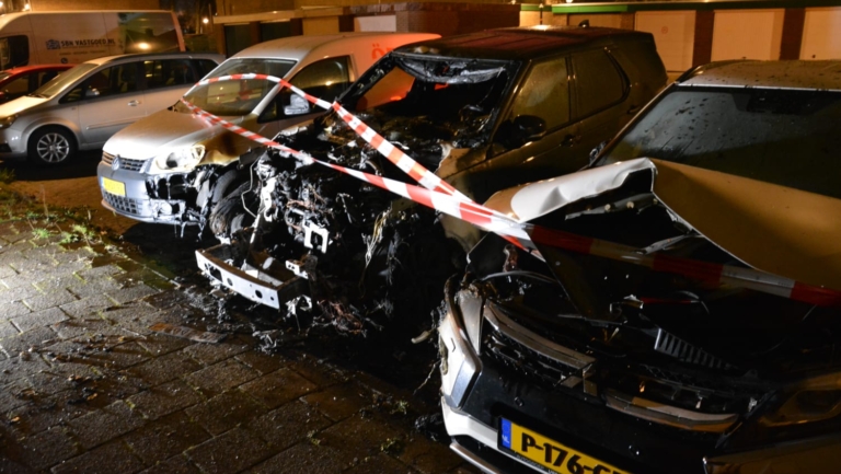 Twee zwaar beschadigde auto's met rood-wit lint eromheen, vermoedelijk na een brand.