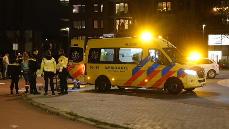 Een ambulance en politieagenten op een rotonde bij nacht, met zwaailichten aan.
