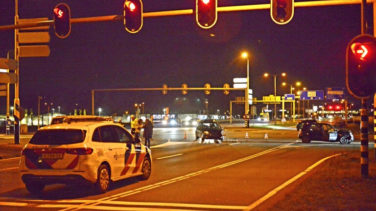 Verkeersongeval bij nacht met politievoertuig en beschadigde auto's op kruispunt.