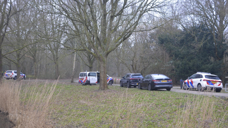Politievoertuigen geparkeerd langs een bospad met kale bomen.