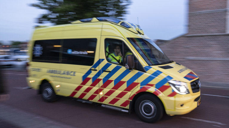 Geel-rode ambulance met zwaailichten aan rijdt over straat.