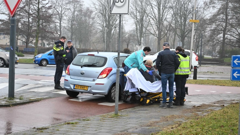 Een ongeluksscène met een auto en een brancard, omringd door hulpverleners en politieagenten.