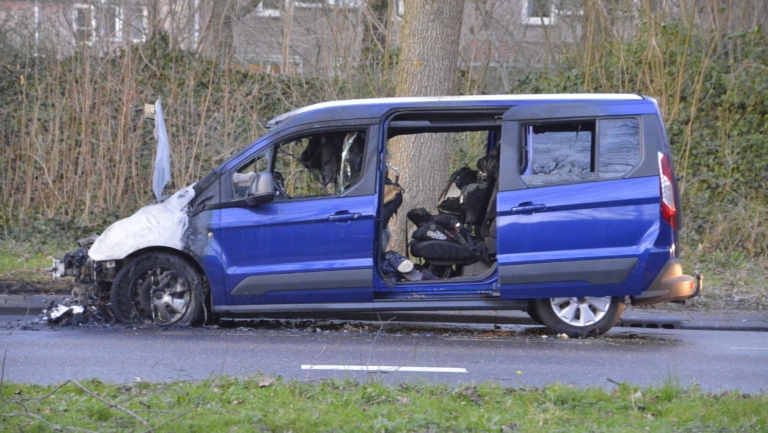 Een blauwe auto met zware brandschade aan de voorzijde staat naast een boom.
