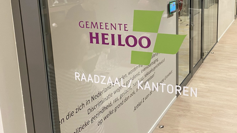 Glazen deur met het logo en de tekst van de gemeente Heiloo, en de woorden 'Raadzaal KANTOREN', met een fragment van artikel 1 van de Nederlandse grondwet over discriminatie daaronder.