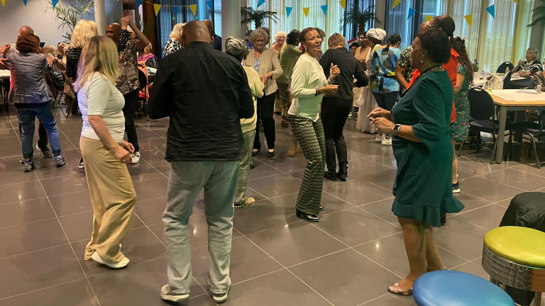 Mensen dansen samen op een feestelijke bijeenkomst in een zaal met feestelijke vlaggen en zitgelegenheden.