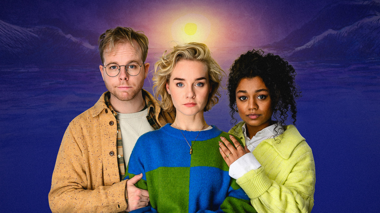 Drie mensen staan voor een achtergrond met een ondergaande zon en bergen. De persoon links draagt een beige jas en bril, de persoon in het midden heeft blond haar en een blauw-groene trui, en de persoon rechts draagt een gele trui en heeft krullend haar.
