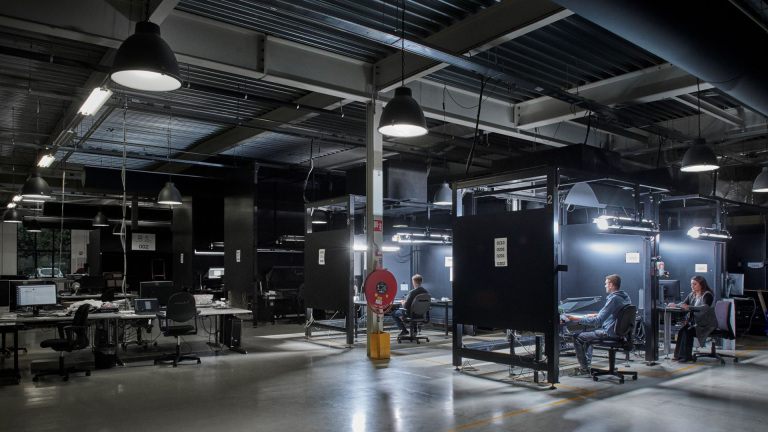 Een moderne kantoorruimte met gedimde verlichting, waar meerdere mensen achter computers werken in aparte cabines en open bureaus.