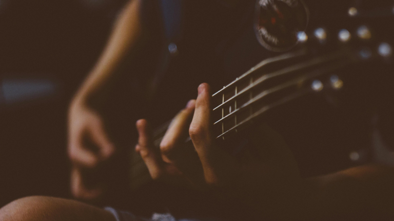 Close-up van een persoon die een basgitaar bespeelt, met de nadruk op de snaren en het fretbord.