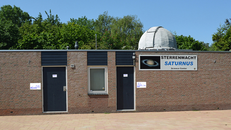 Bakstenen gebouw met de naam "Sterrenwacht Saturnus" op een bord, uitgerust met een koepelvormig observatorium.