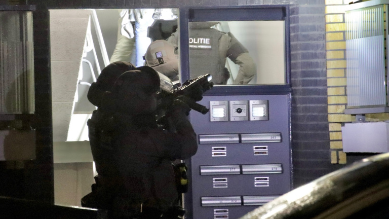 Gewapende politieagenten met speciale uitrusting voor een gebouw met postvakken, tijdens een operatie.