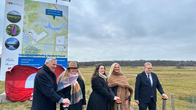 Vijf mensen staan buiten voor een bord dat het project Gebiedsontwikkeling Zanderij Noord aankondigt.