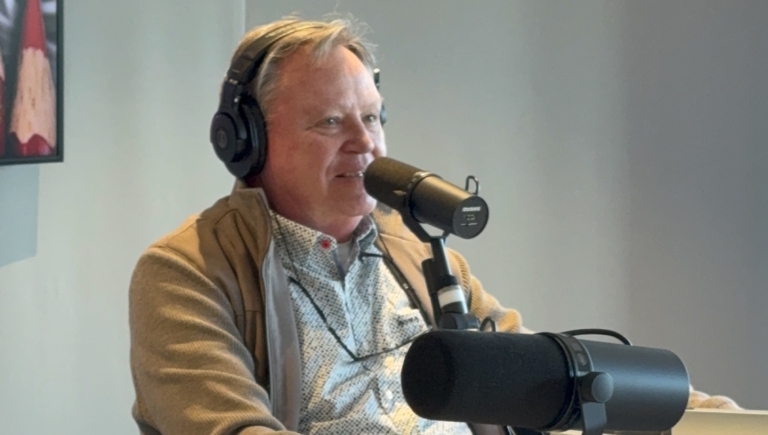 Man met koptelefoon praat in een microfoon in een opnamestudio, met een gele dobbelsteen op de tafel.