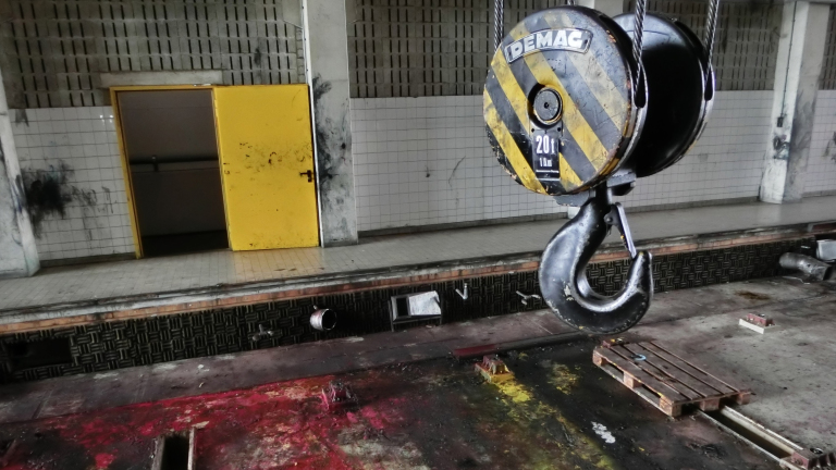 Grote hijshaak met het opschrift "20T" in een oude industriële ruimte met een gele deur op de achtergrond.