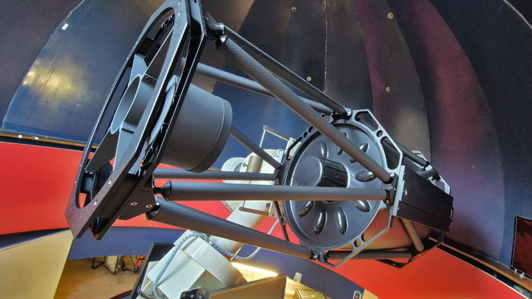 Een grote telescoop met een complexe structuur in een observatorium met gekleurde muren.