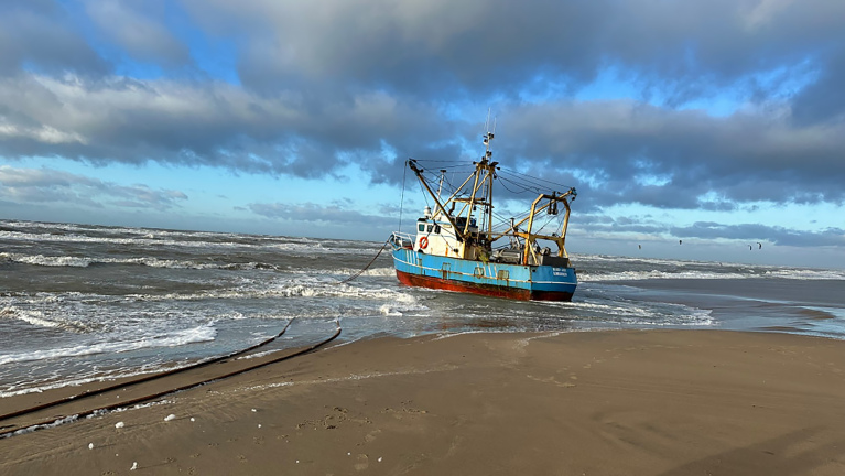 Een vissersboot gestrand op een zandstrand met golven en een bewolkte lucht op de achtergrond.
