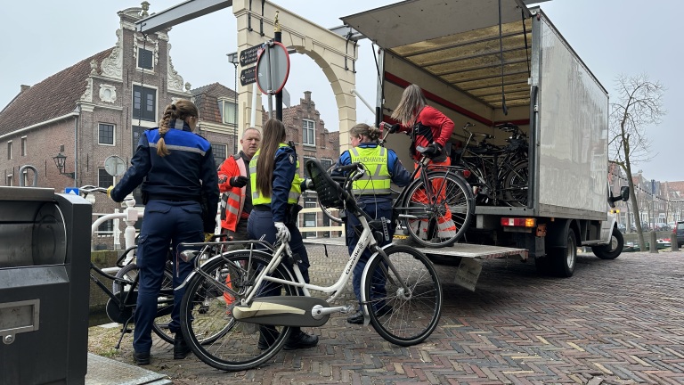 Handhavingsambtenaren laden fietsen in een vrachtwagen naast een historische gevel in een Nederlandse straat.