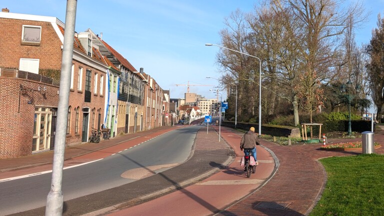 Fietser op een rustige straat met rode fietspaden, omgeven door oude gebouwen en bomen op een zonnige dag.