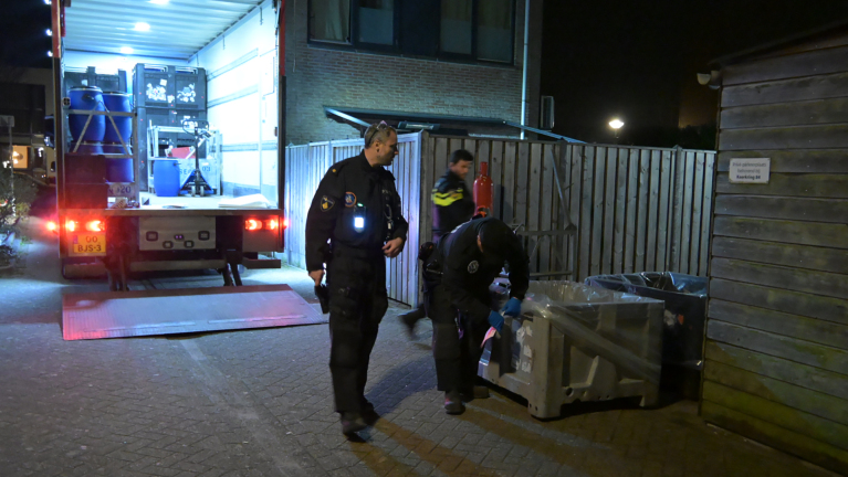 Politieagenten onderzoeken 's nachts een container bij een geopende vrachtwagen op een rustige straat.