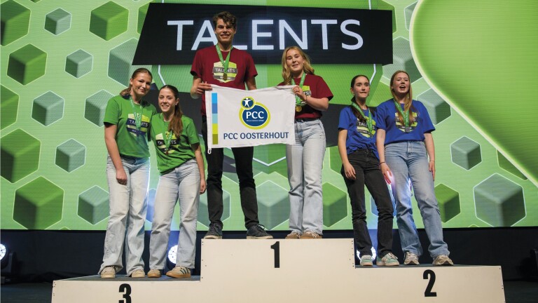 Zes jongvolwassenen staan op een podium met een banner van PCC Oosterhout; ze dragen medailles en gekleurde shirts.