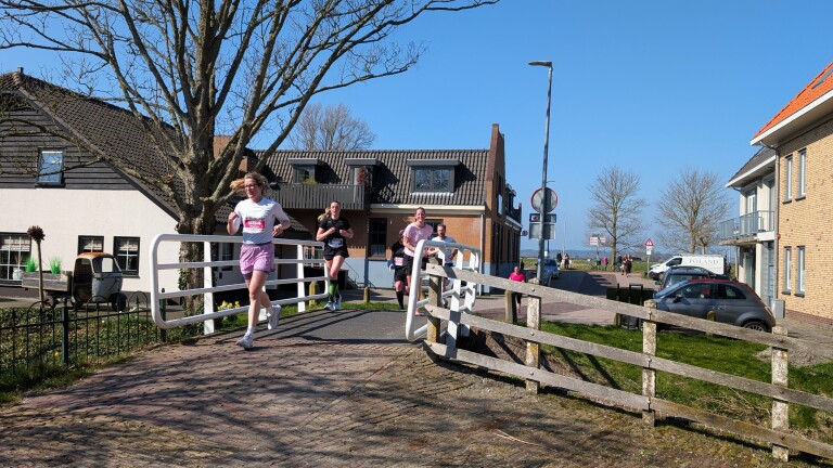 Mensen rennen over een brug in een woonwijk op een zonnige dag met een blauwe lucht.