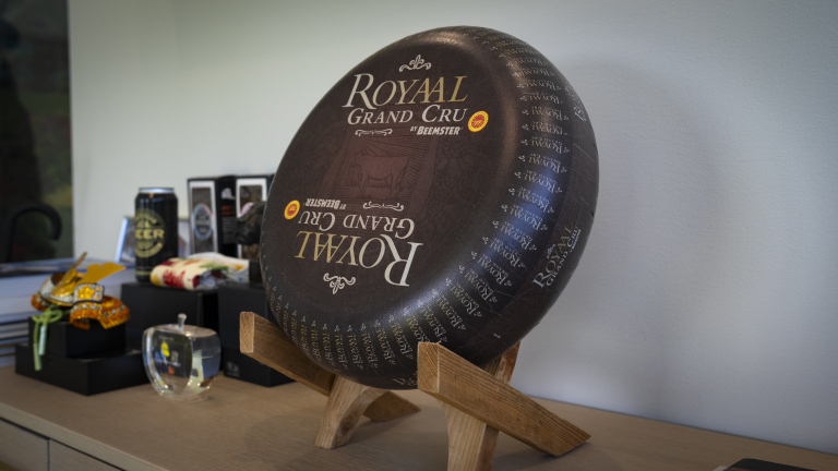 Een grote ronde kaas met de tekst "Royaal Grand Cru by Beemster" op een houten standaard, omringd door diverse cadeauartikelen.