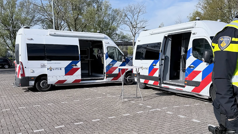 Twee geopende politiebusjes staan geparkeerd op een plein, met een agent zichtbaar aan de rechterkant.