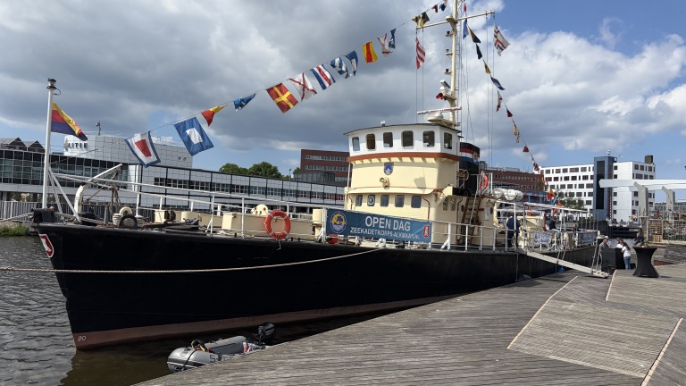 Een schip versierd met vlaggen ligt aangemeerd bij een kade tijdens een open dag van het Zeekadetkorps.