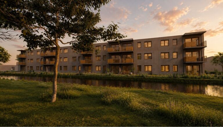 Appartementengebouw bij zonsondergang weerspiegeld in een rustige vijver, omgeven door een grasveld en bomen.