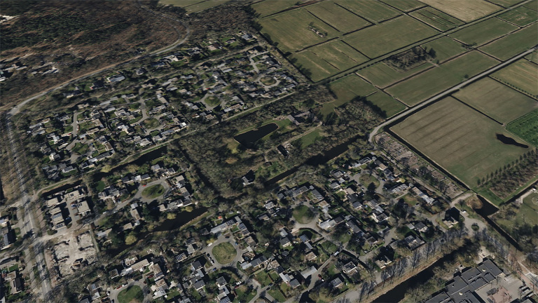 Luchtfoto van een woonwijk, omgeven door groene landbouwvelden en bossen.