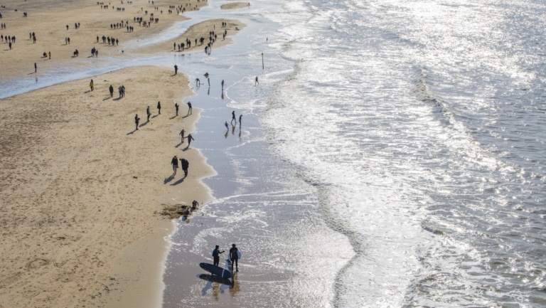Mensen wandelen en spelen op een zonnig strand langs de waterlijn.