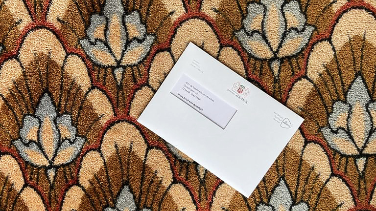 Een witte envelop met een adressticker ligt op een kleurrijk, bloemvormig tapijt.