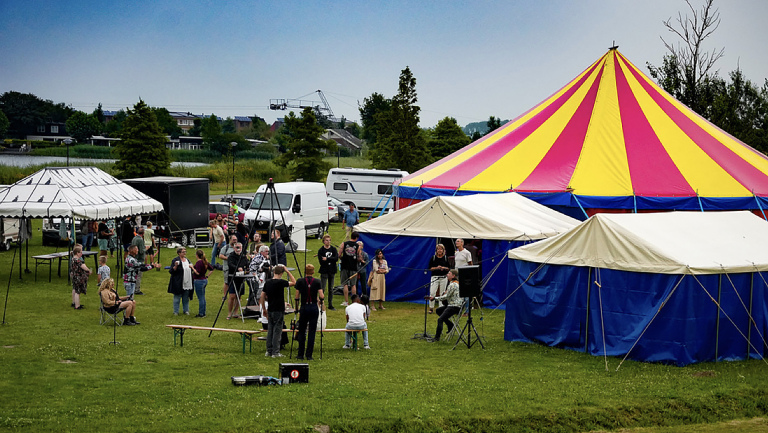 Kleurrijke circustent met mensen eromheen op een grasveld, samenkomend voor een evenement.