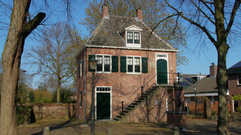 Bakstenen huis met groen luiken, buitentrap naar voordeur en straatlantaarn, omringd door bomen