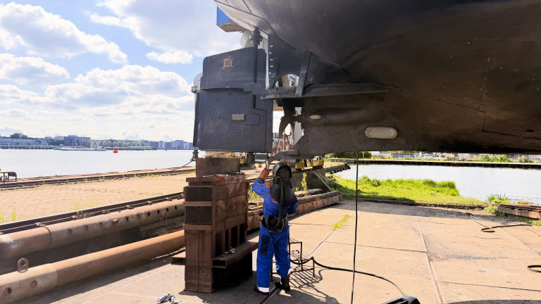 Monteur in blauwe overall werkt onder de romp van een schip op een werf langs het water