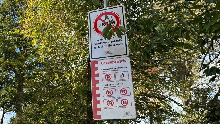 Verkeersbord in park met verboden drugs en gedragsregels tegen overlast, tussen groene bomen