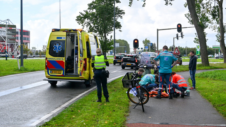 Ambulance en politie bij kruispunt; hulpverleners behandelen persoon op fietspad naast een omgevallen fiets