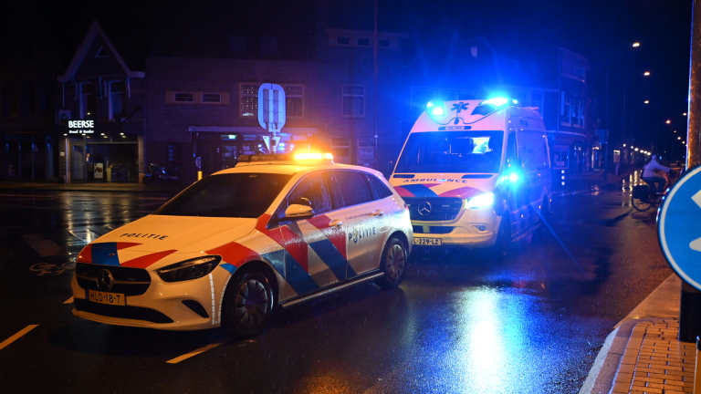 Politiewagen en ambulance met zwaailichten op een natte straat in de nacht, met gebouwen op de achtergrond