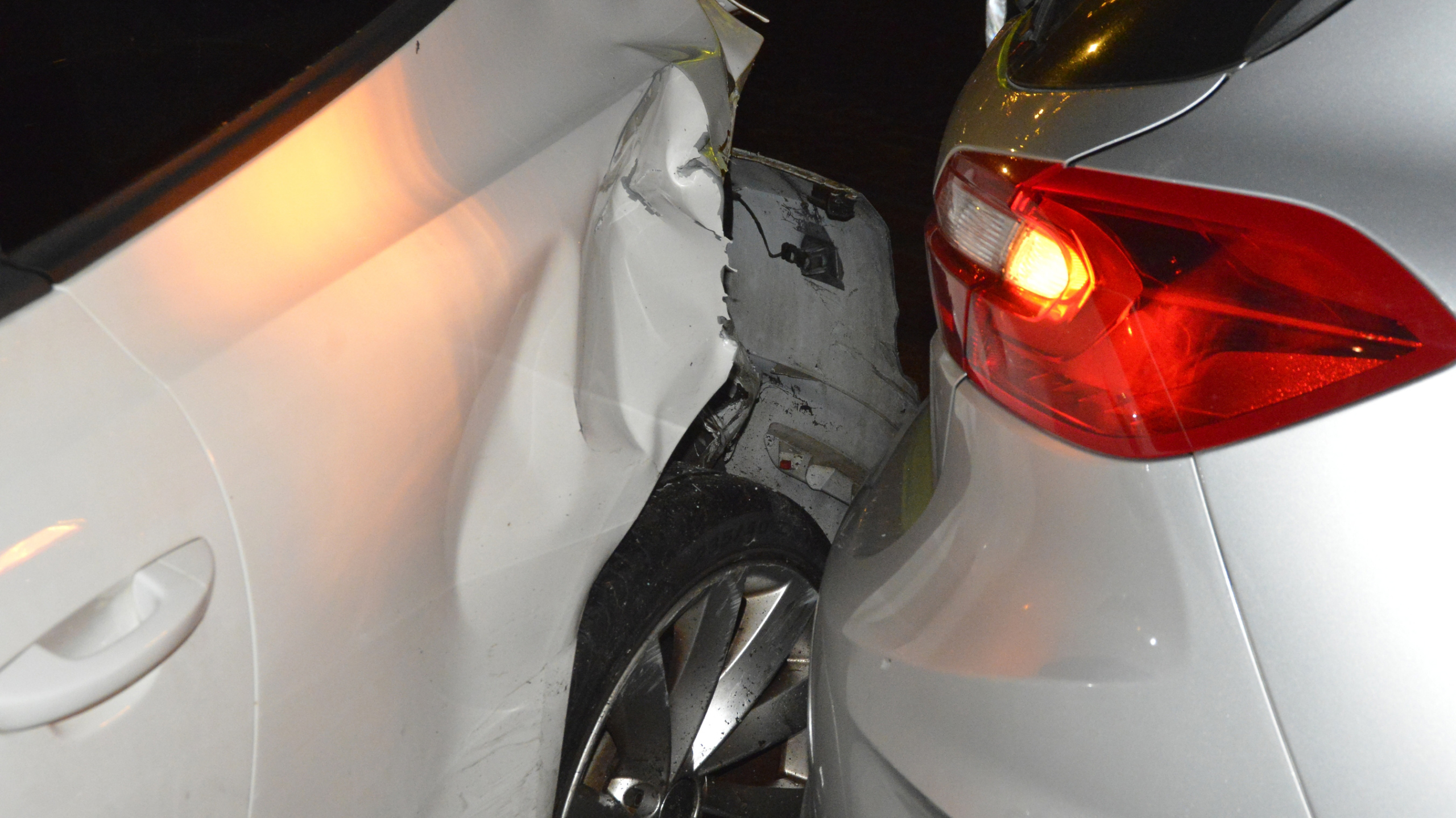 Twee auto's betrokken bij een botsing op een straat 's nachts, met zichtbaar schade aan de voorzijde van de zilveren auto.