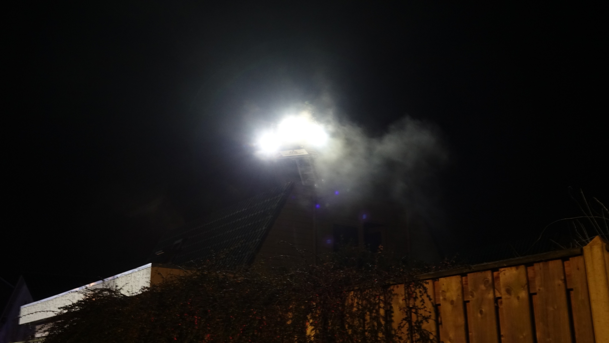 Brandweerauto met ladder in actie bij nacht naast een kerk, omgeven door woonhuizen.