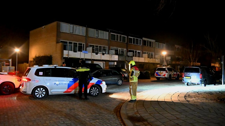 Politie- en brandweervoertuigen staan geparkeerd in een woonstraat 's nachts, met een politieagent en brandweerman aanwezig.
