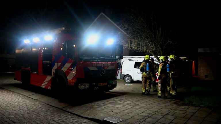 Politie- en brandweervoertuigen staan geparkeerd in een woonstraat 's nachts, met een politieagent en brandweerman aanwezig.