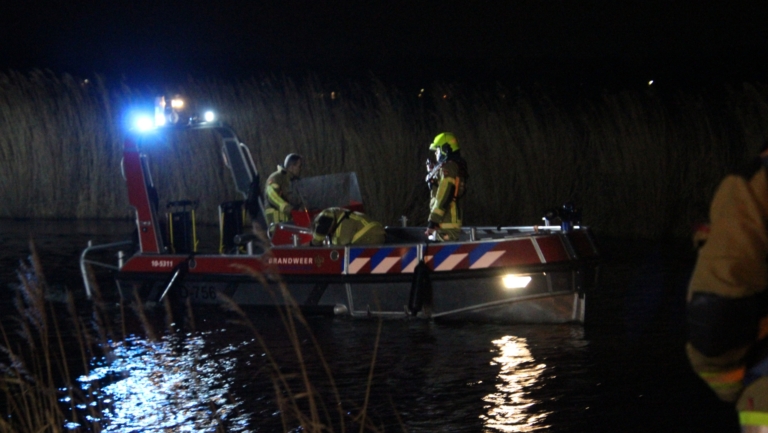 Brandweerlieden op een reddingsboot uitvoeren een nachtelijke operatie op een meer, verlicht door felle lichten.