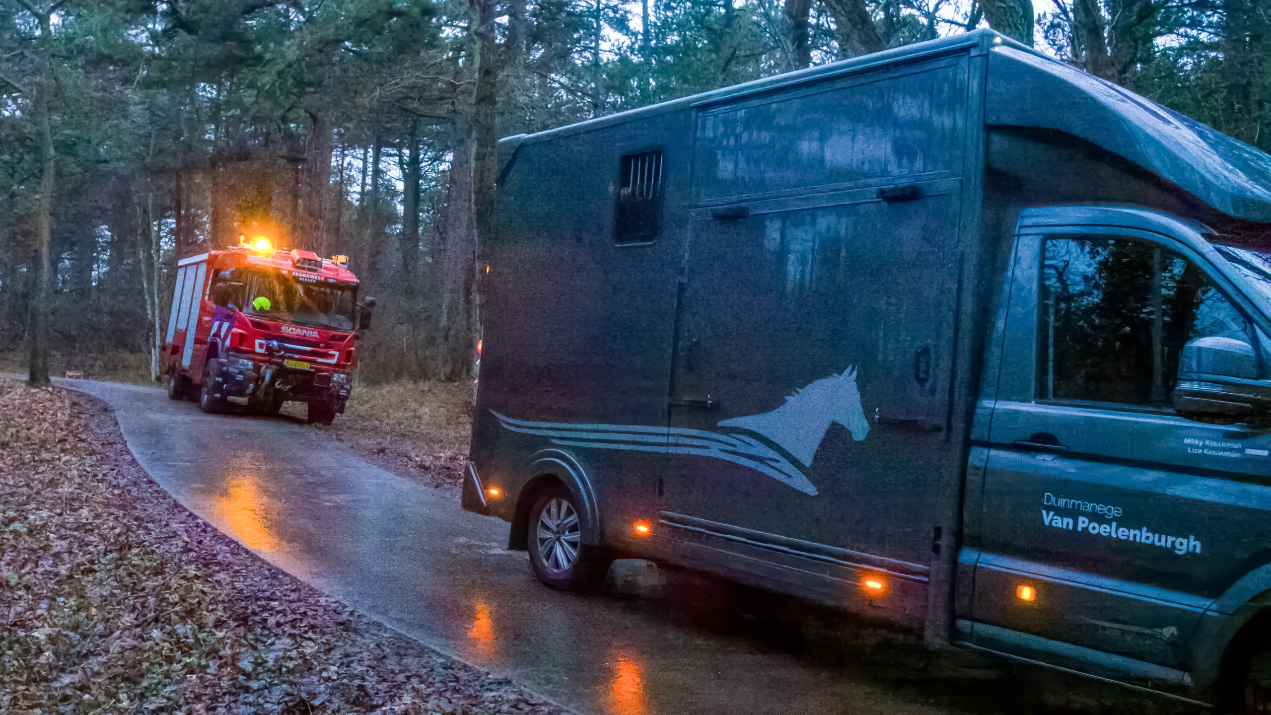 Brandweerlieden en mensen lopen op een modderig bospad omringd door dichte bomen.