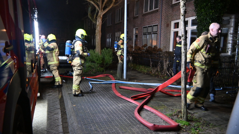 Een schuur met brandschade, gevuld met fietsen en houtblokken, met aan de rechterkant een groene zeilafdekking.