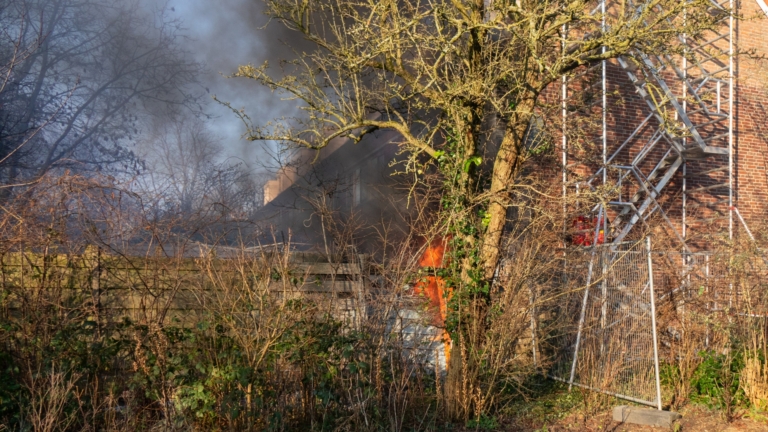 Brandweermannen bestrijden een woningbrand met een brandweerwagen en uitrusting, omgeven door rook.