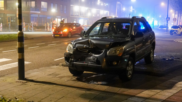 Twee ambulances en hulpverleners staan bij een rode auto met schade na een ongeval op een kruispunt 's nachts.