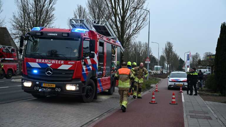 Brandweerman op een ladder controleert een schoorsteen op het dak van een huis terwijl hij beschermende kleding en een helm draagt.
