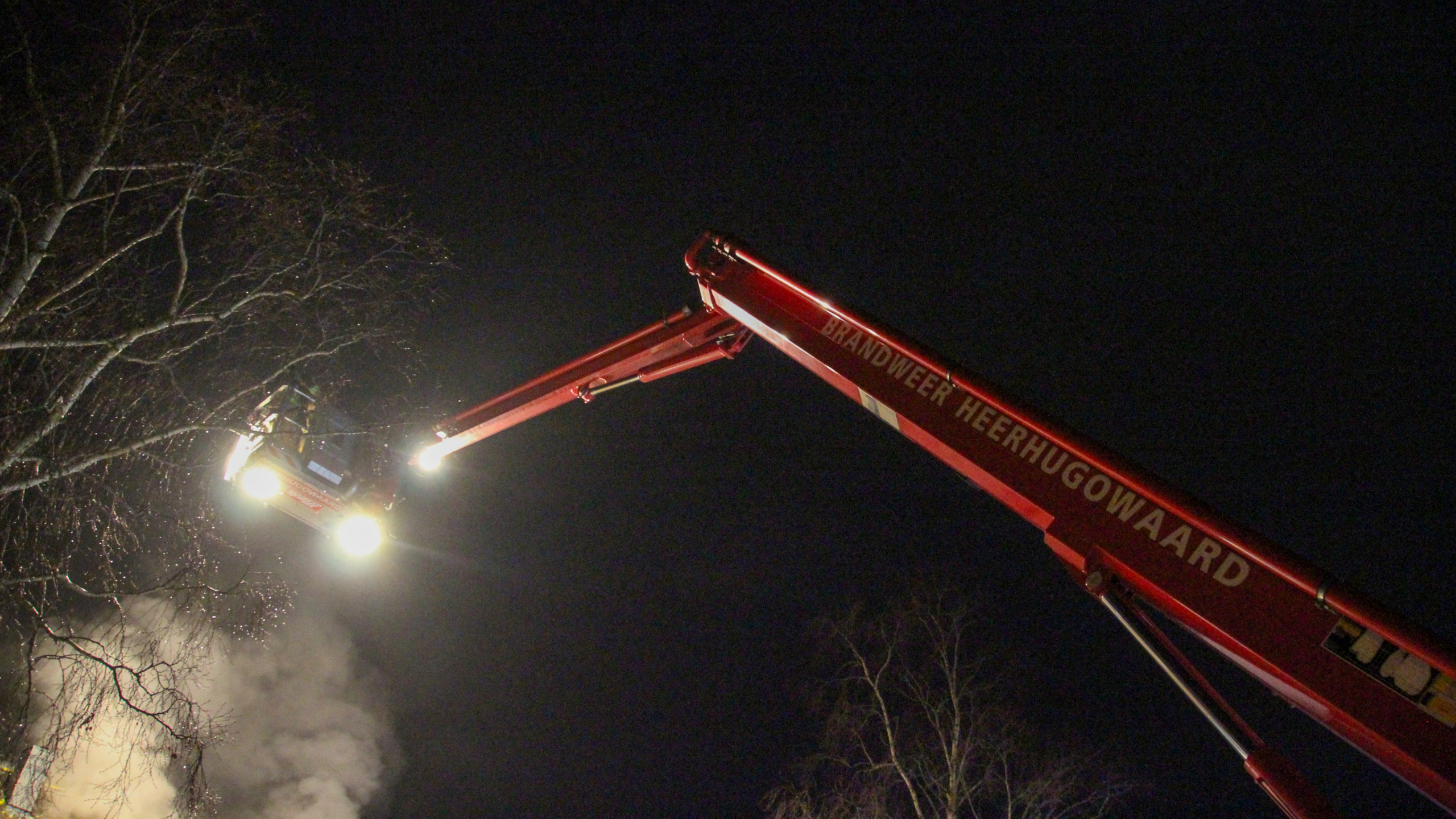 Rook komt uit het dak van een rijtjeshuis onder een donkere hemel.
